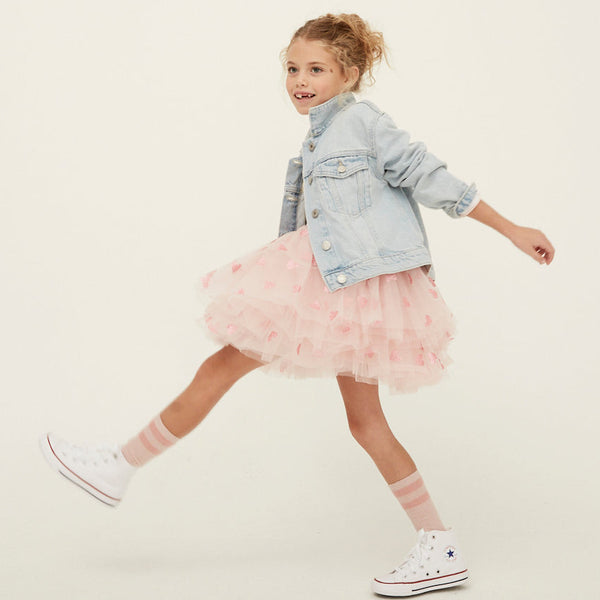 Child wearing a denim jacket and pink tutu skirt on a plain background