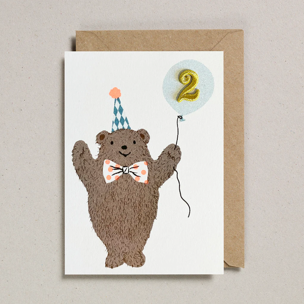 Birthday card with a bear holding a number two balloon and a party hat on a beige background